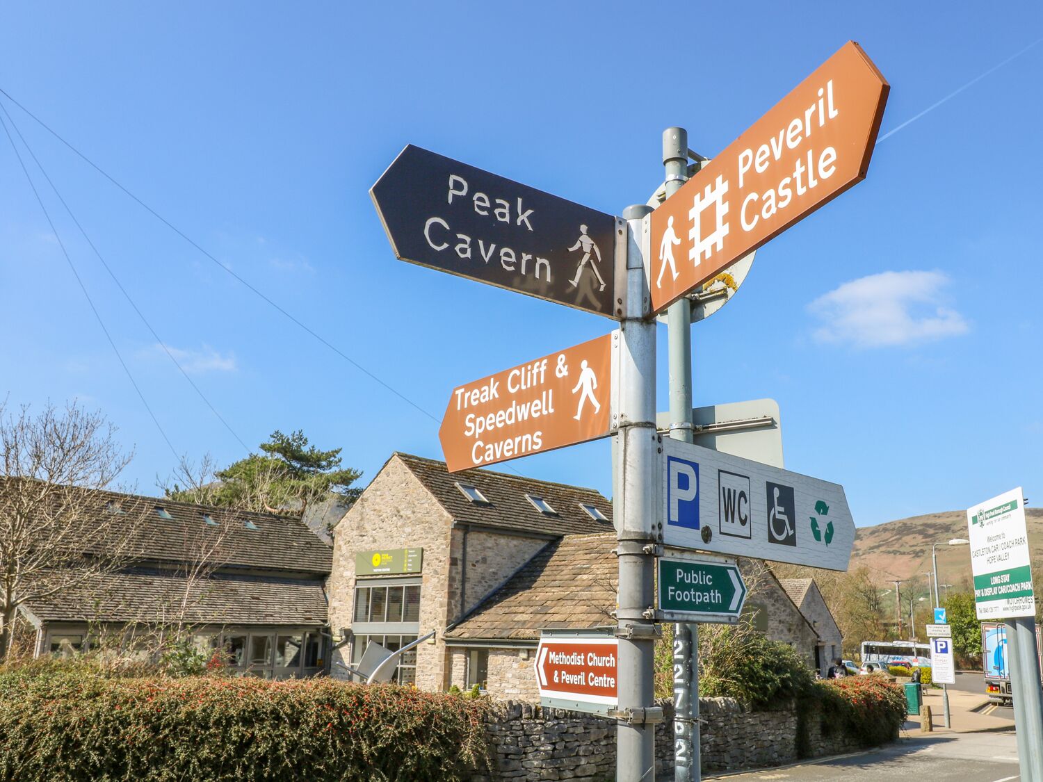 Un panneau indicateur directionnel avec de nombreuses flèches pointant vers différentes destinations, notamment les grottes de Peak Cavern, de Treak Cliff et de Speedwell, ainsi que le château de Pewerl.