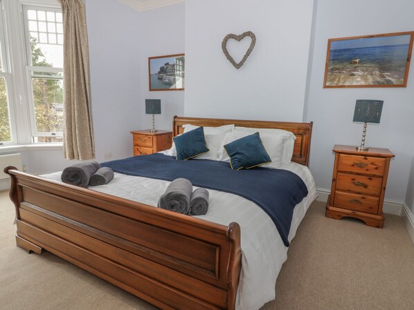 Una cama bien hecha con toallas enrolladas, una decoración con forma de corazón en la pared y un cuadro con una escena de playa.
