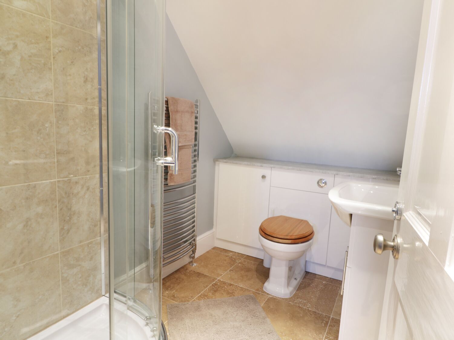Ein Badezimmer mit Duschkabine aus Glas, Toilette mit Holzsitze und einem weißen Waschbecken.