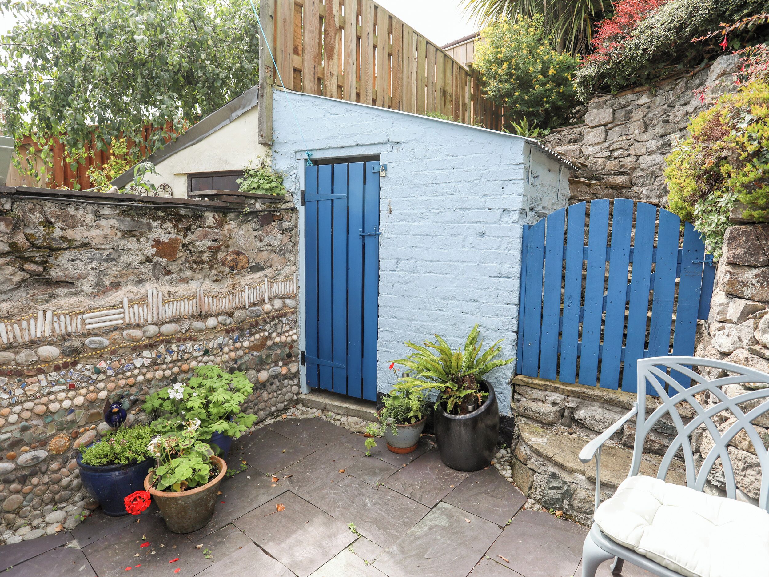 Un petit espace extérieur clos, avec un mur en pierre, une porte bleue et des plantes en pot.