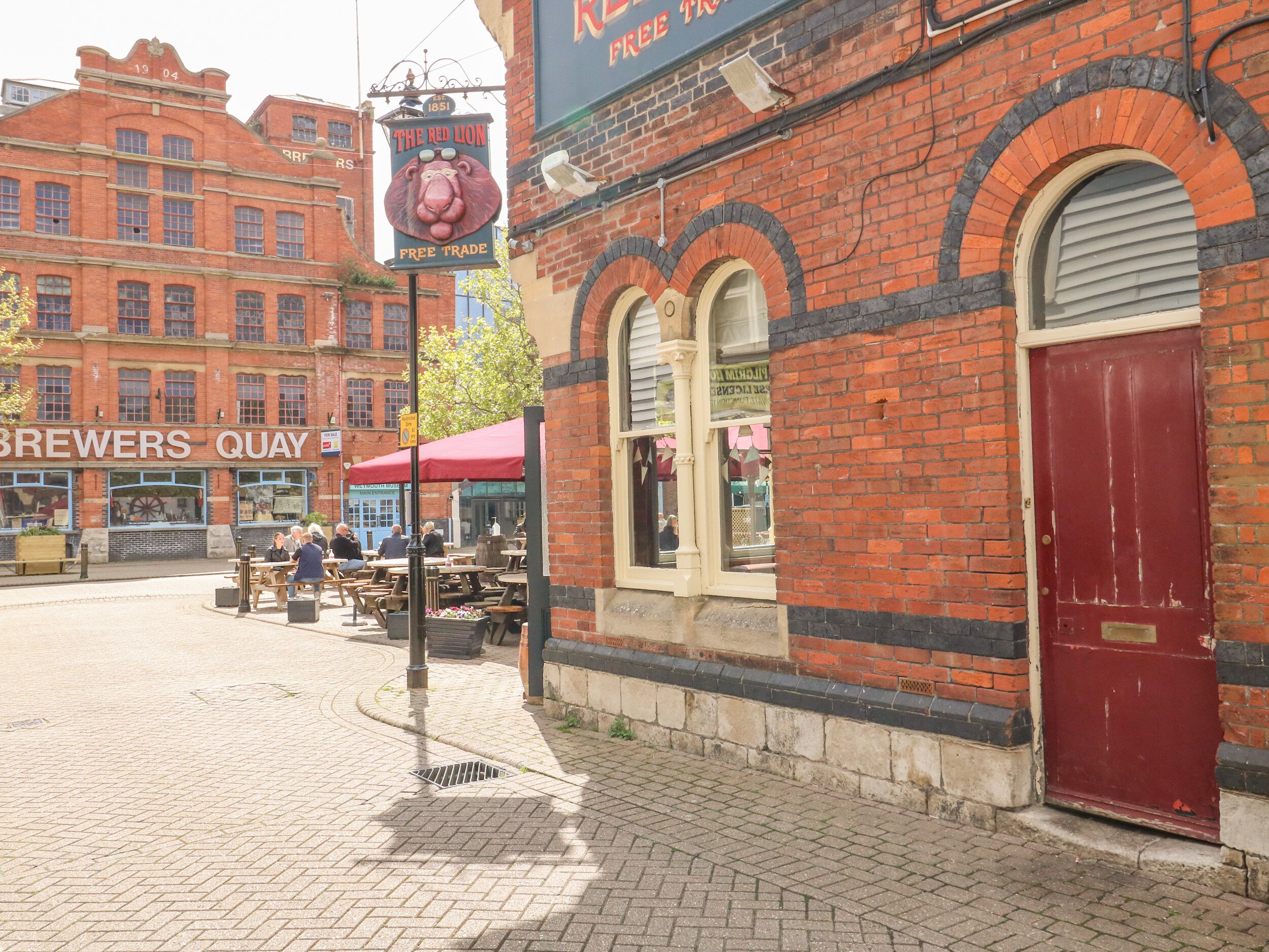 A brick building with a red door, a sign for 'The Red Lion' pub, and outdoor seating.