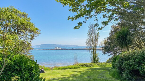 A grassy area with a view of a calm body of water and distant landforms. - Maisy Cottage (Weymouth)