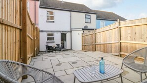 A patio area with a table and chairs, a wooden fence, and a building in the background. - Maisy Cottage (Weymouth)