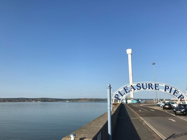 A bridge with a sign reading "Pleasure Pier" and a view of the water and distant land.