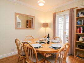 Un comedor con una mesa de madera dispuesta para seis personas, un espejo en la pared, una estantería con libros y una lámpara.