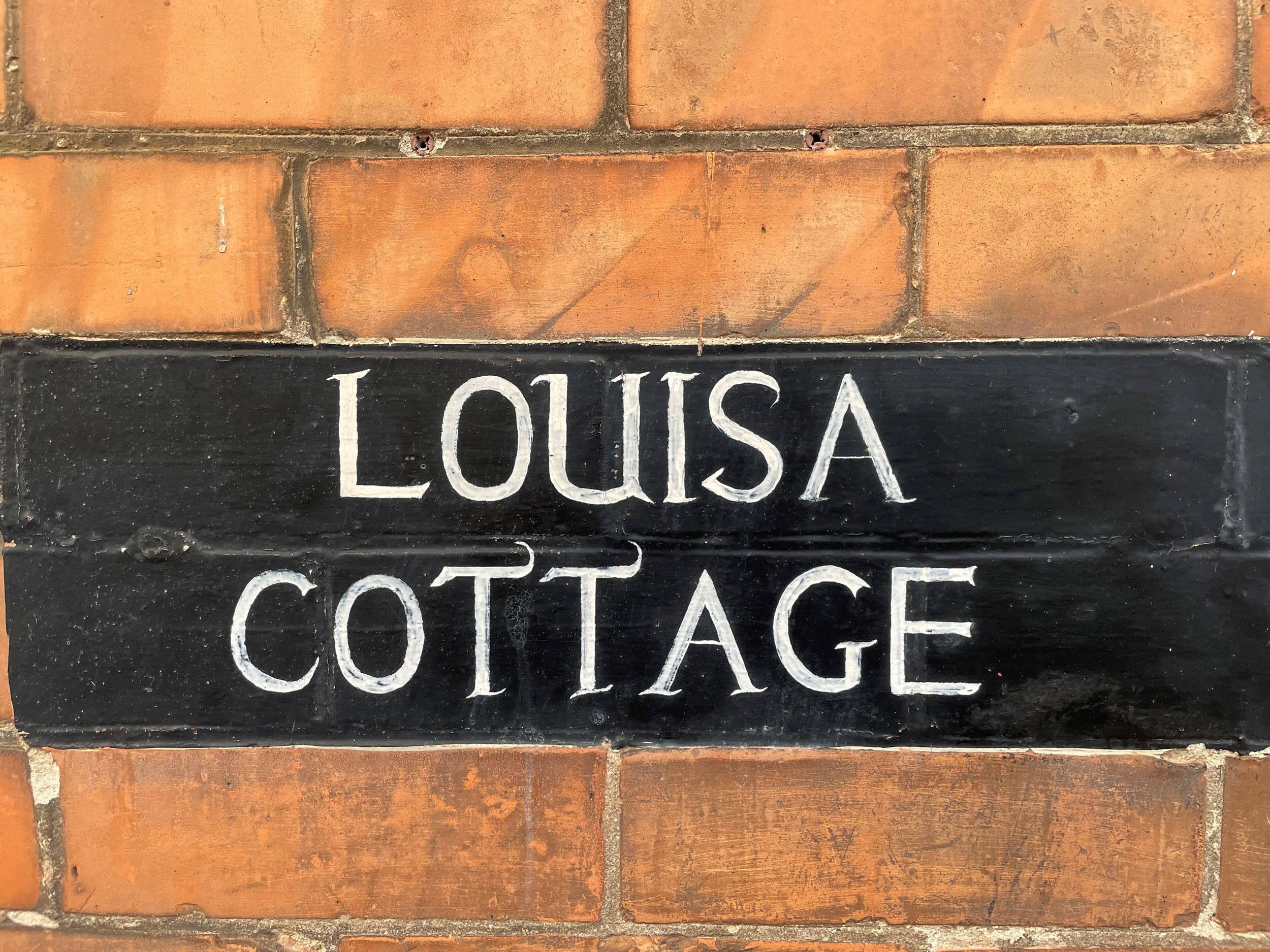 A black sign with white lettering that reads "LOUISA COTTAGE".