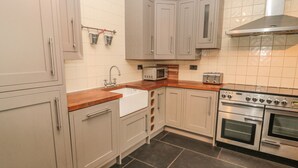 A kitchen with grey cabinets, a wooden countertop, a stainless steel range hood, a microwave, a toaster, and a double oven. - Hare &amp; Hounds House (Hexham)