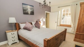 A bedroom with a wooden bed, white nightstands, a chandelier, a window with curtains, and a view of a brick wall. - Hare &amp; Hounds House (Hexham)