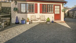 Ett litet hus med en grusuppfart, två trästolar och krukväxter.