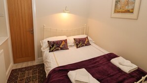 Un dormitorio con cama, almohadas, una colcha, una puerta y un cuadro en la pared.