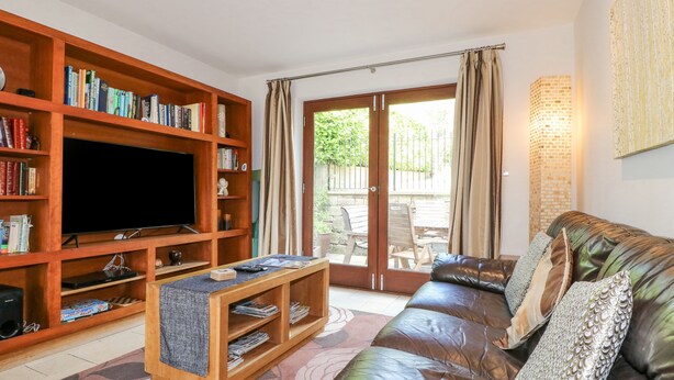 A living room with a leather sofa, a wooden entertainment unit with books, a flat-screen TV, and a coffee table. - Torestyn (Matlock)