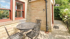 A stone building with a window and a door, a metal table and chairs, and a small garden area with a metal railing. - Torestyn (Matlock)