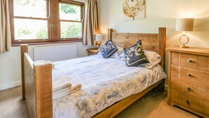 A bedroom with a wooden bed, a nightstand with a lamp, a radiator, and a window with curtains. - Torestyn (Matlock)