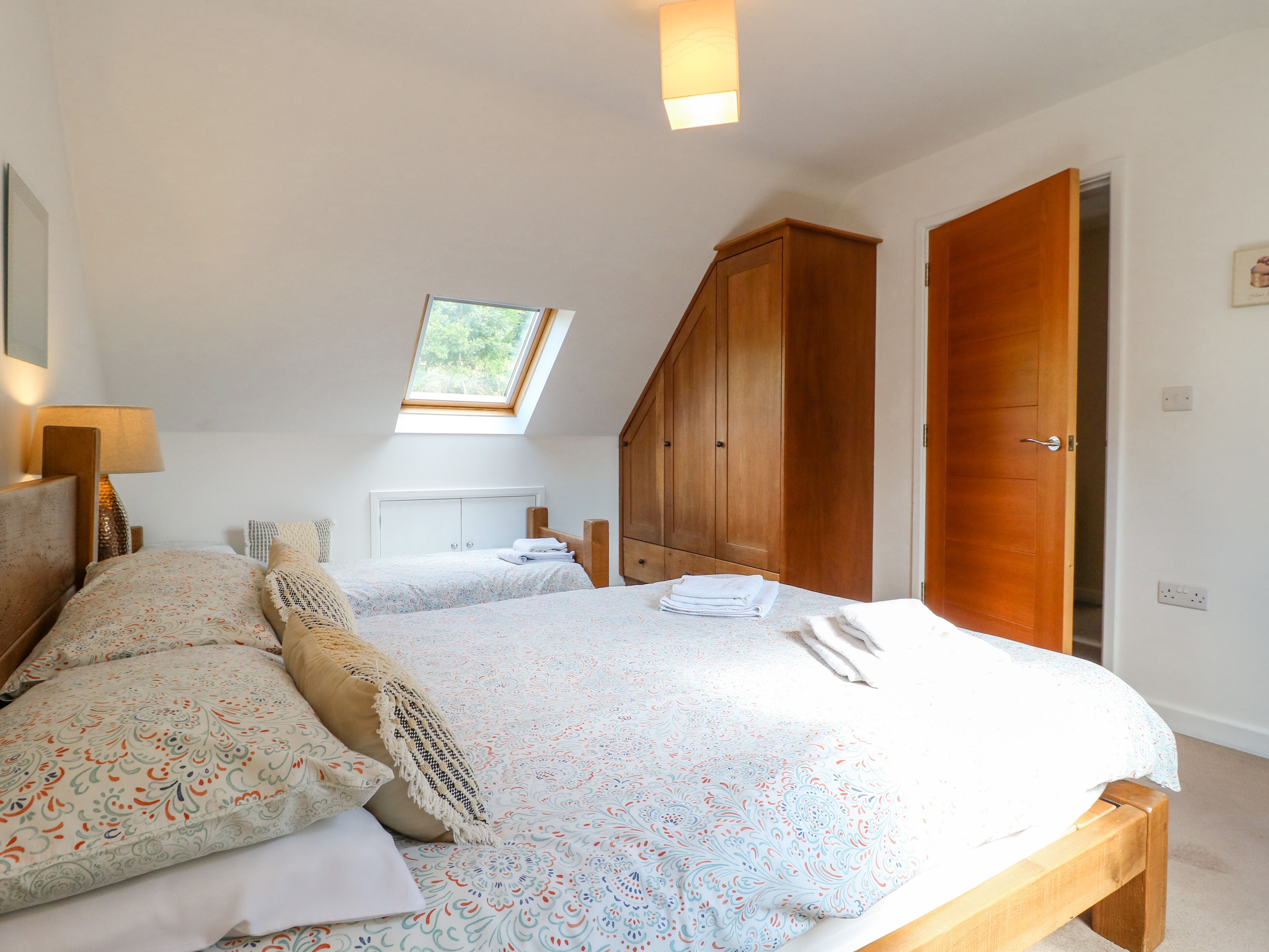 Un dormitorio con una cama grande, tragaluz, armario de madera y una puerta.