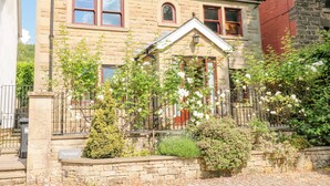 A two-story stone house with a gabled roof, a front porch, and a small garden with flowering plants. - Torestyn (Matlock)