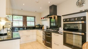 A modern kitchen with a black stove, oven, and microwave, white cabinets, and a window with blinds. - Torestyn (Matlock)