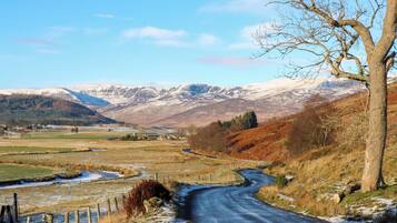 A rural road winding through a hilly landscape with snow patches and a clear sky.