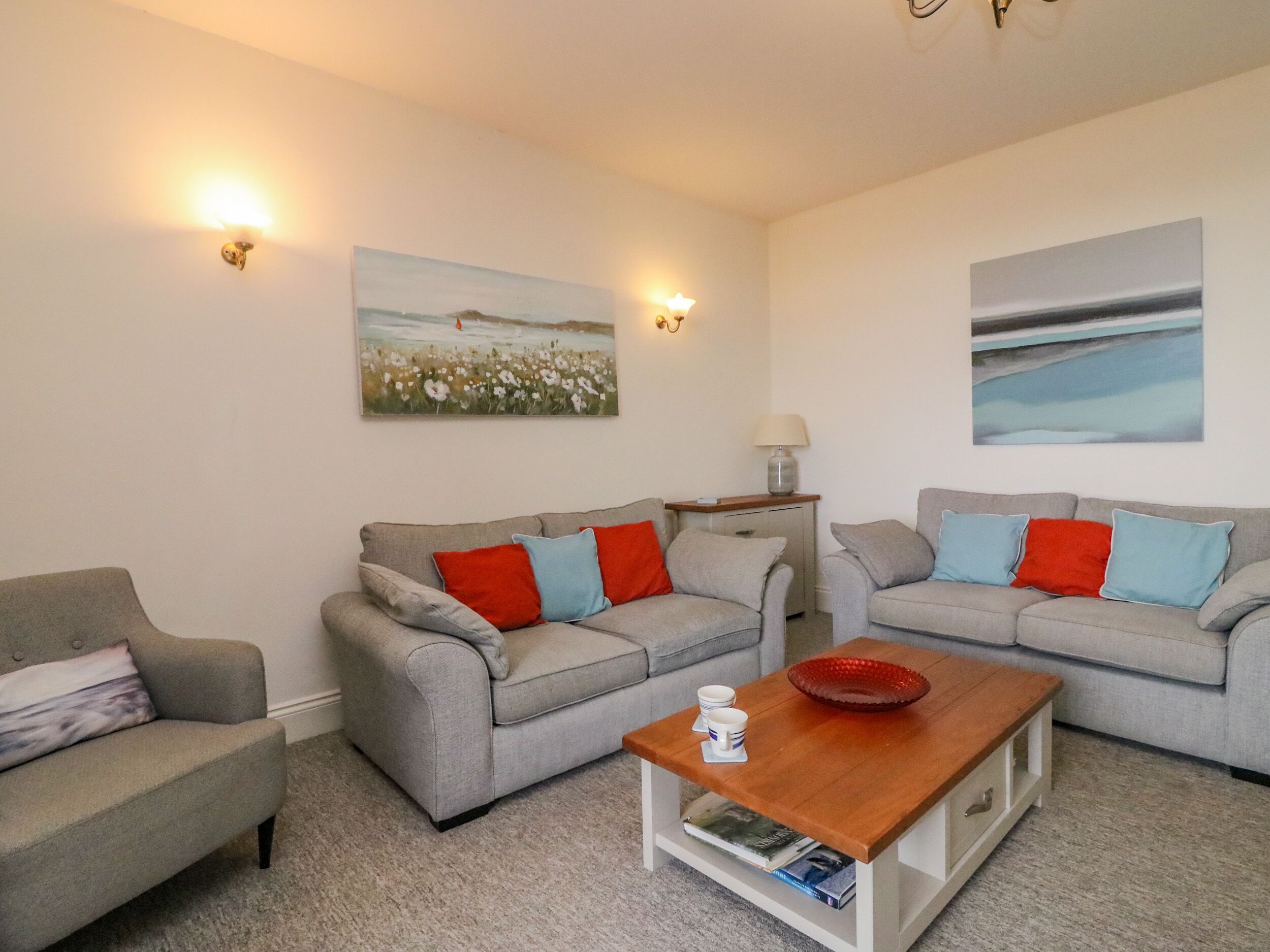 Ein Wohnzimmer mit zwei grauen Sofas, roten und blauen Kissen, einem Holztisch und Wandlampen.