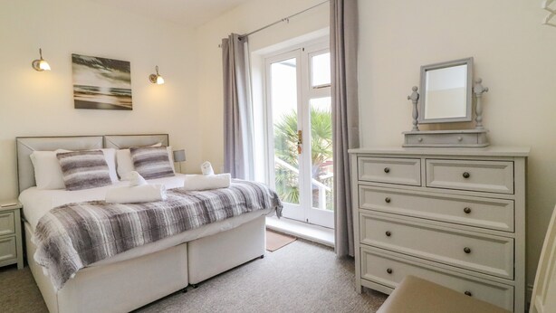Une chambre à coucher avec un lit, des tables de chevet, une commode, un miroir et une fenêtre avec des rideaux.