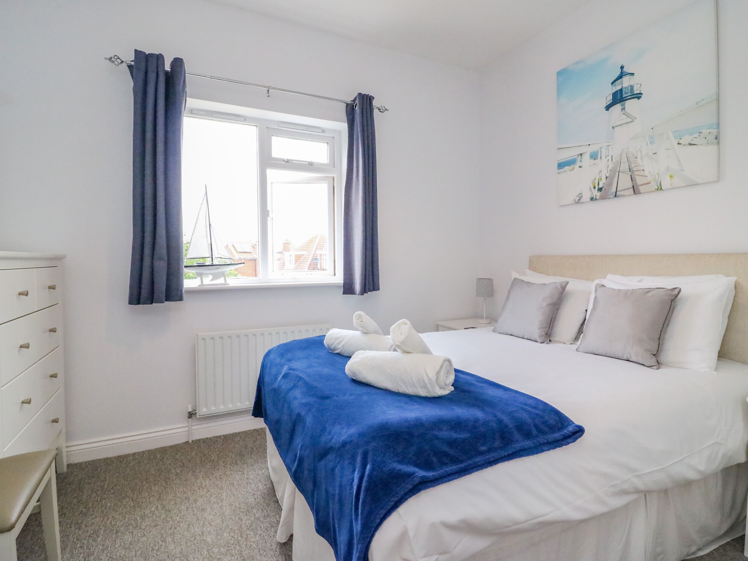Une chambre d’hôtel avec un lit, une commode, une fenêtre avec des rideaux et un tableau représentant un phare.