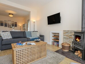 A cozy living room with a sofa, a coffee table, a fireplace, a TV, and a bookshelf. - Bryn Dale (Holyhead)
