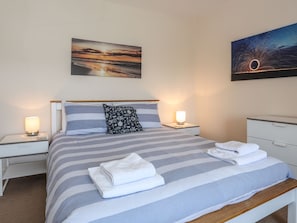 A neatly made bed with striped bedding, two bedside lamps, a pillow, and a folded towel on the bed. - Bryn Dale (Holyhead)