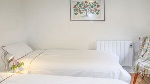 A bedroom with two beds, a radiator, a lamp, and a framed picture on the wall. - Ffrwd Cottage (Bodorgan)