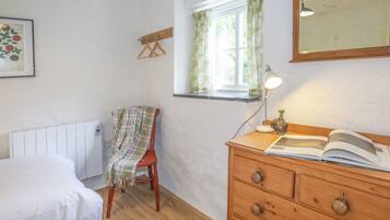 A bedroom with a bed, a wooden dresser, a chair, a radiator, a window with curtains, and a mirror on the wall.