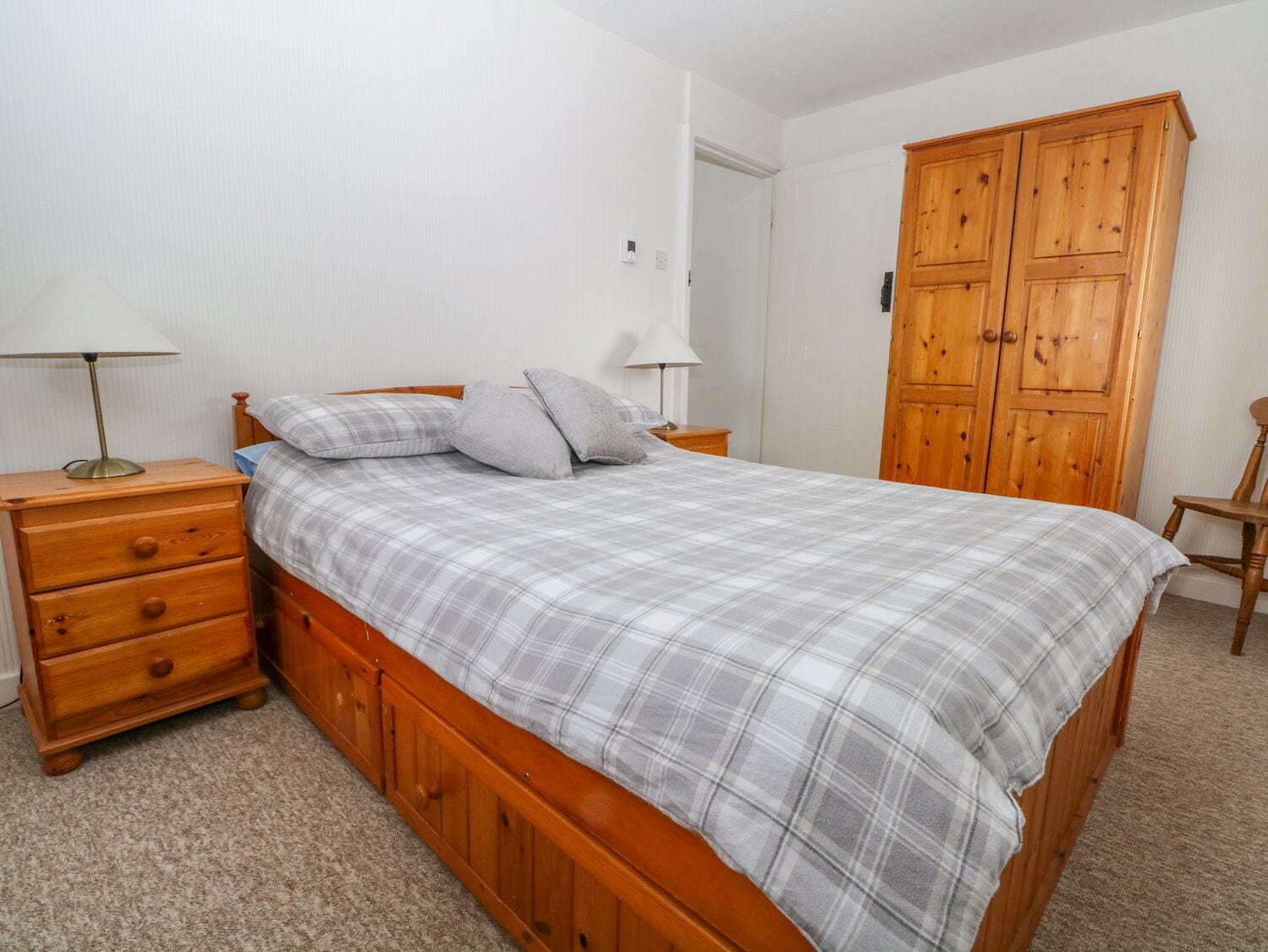 A bedroom with a wooden bed, two bedside tables with lamps, a wooden wardrobe, and a carpeted floor.