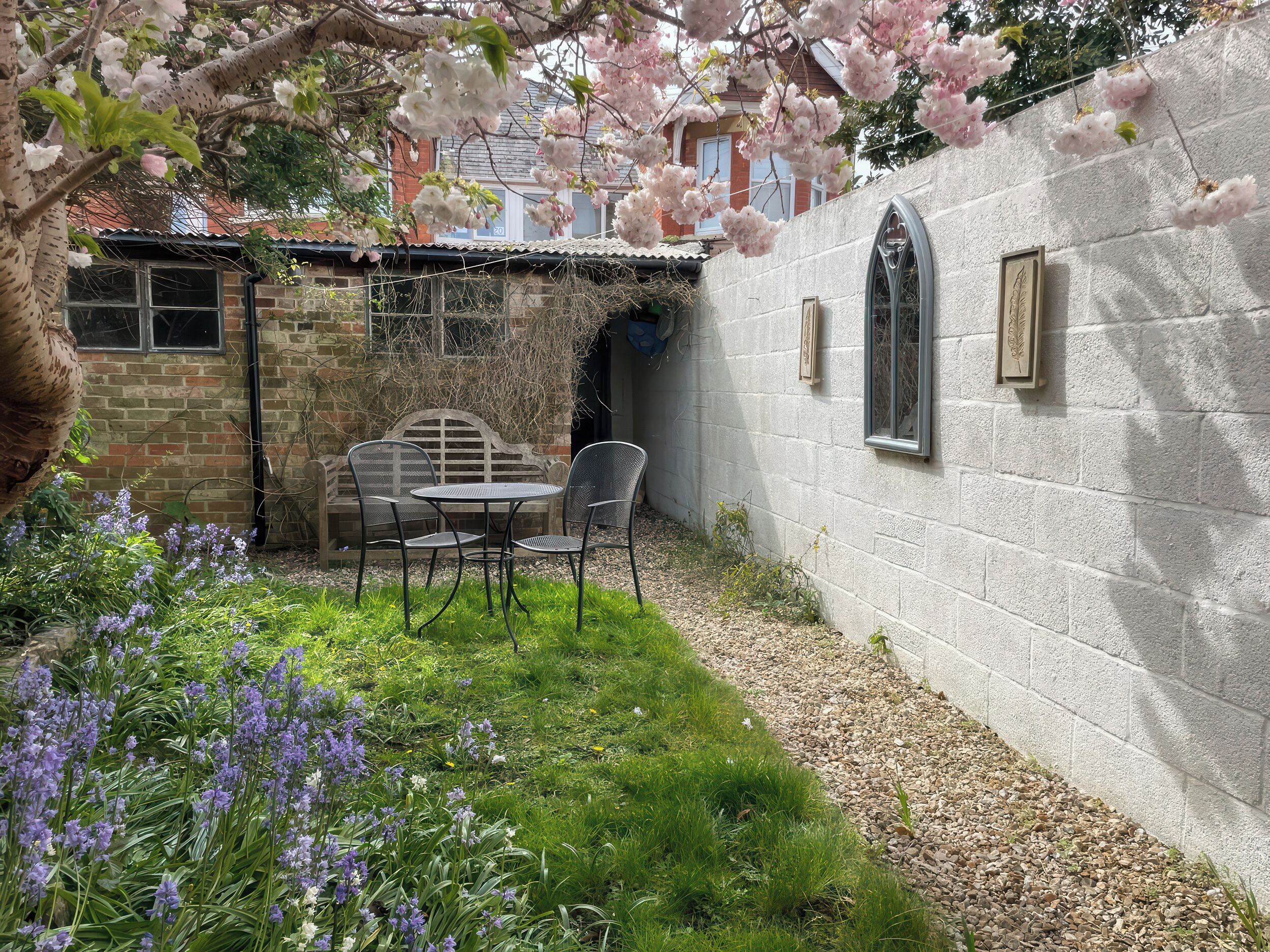 A garden with a table and chairs, a stone wall, and flowering plants.
