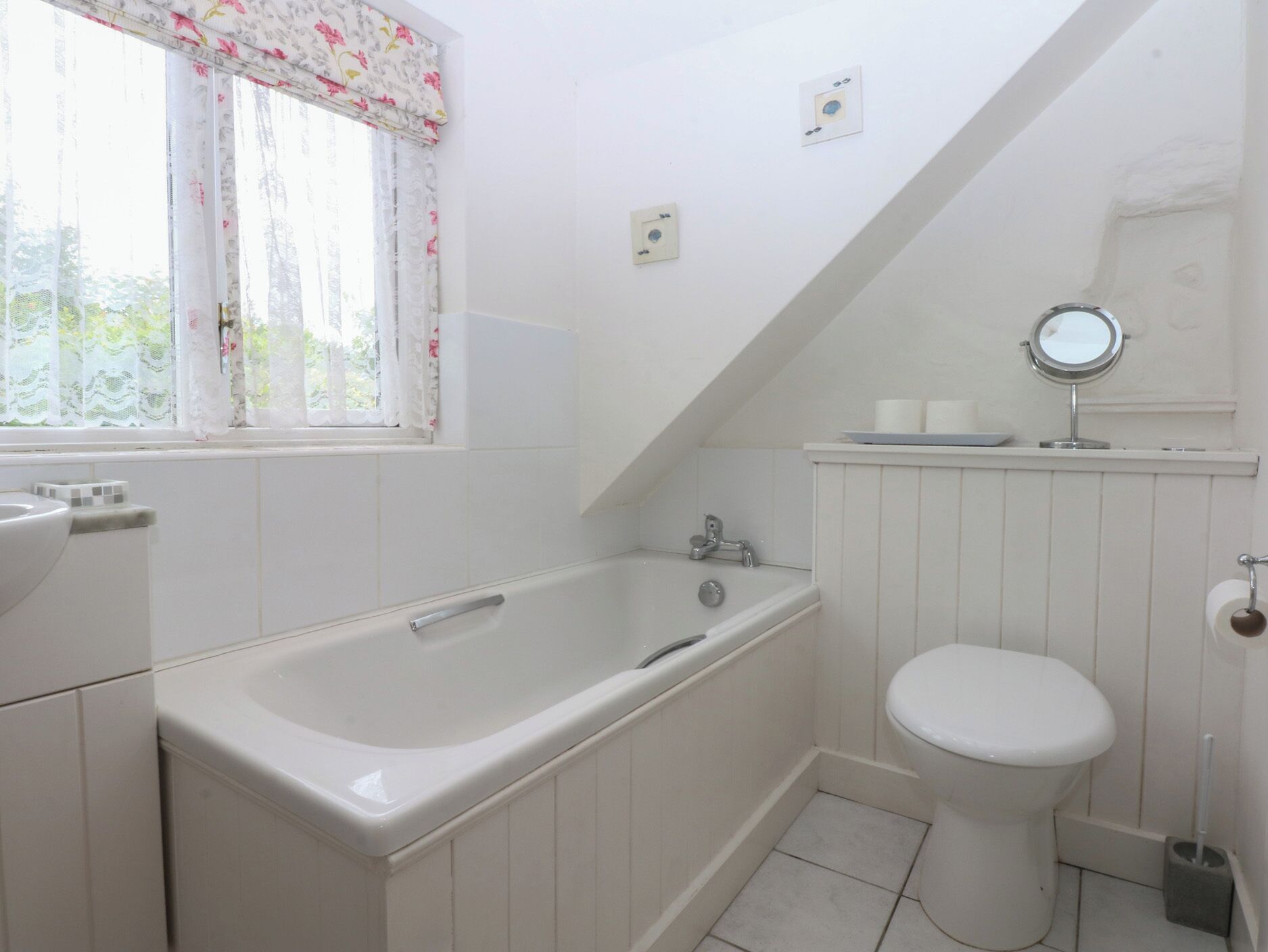 Un baño con bañera, inodoro y ventana con cortinas florales.