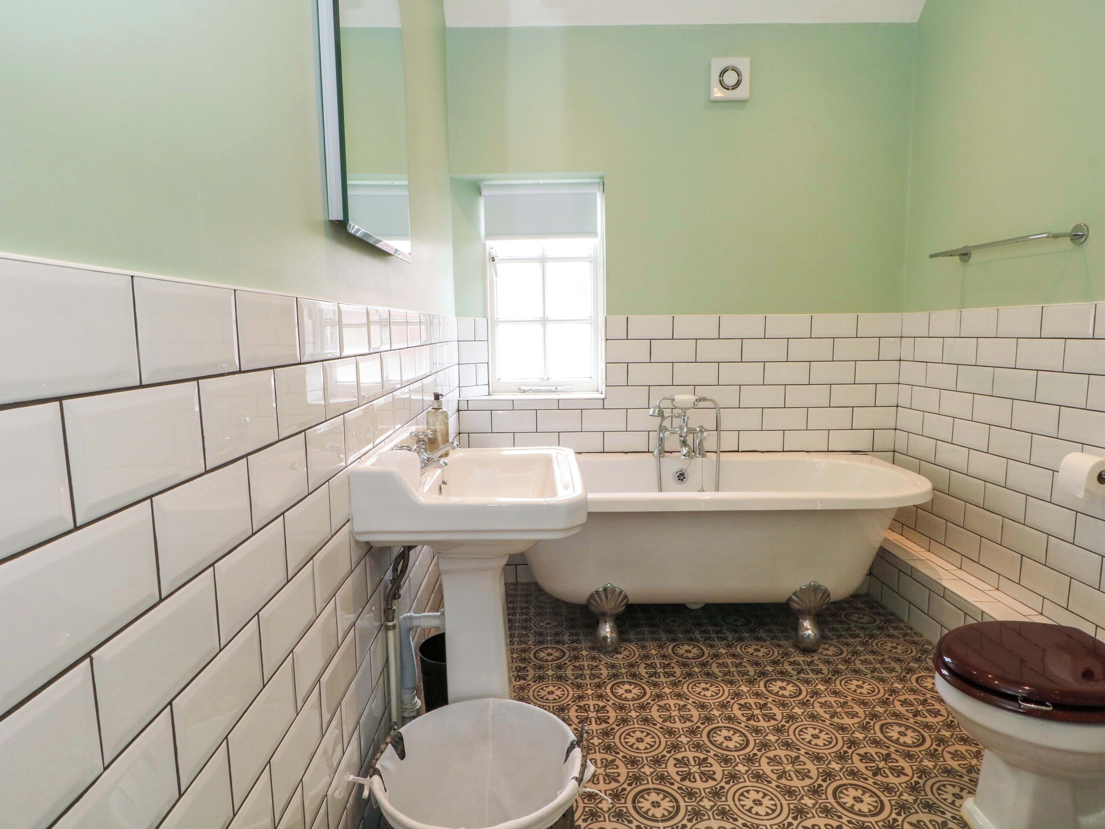 Un baño con azulejos blancos, una bañera, un inodoro y una ventana.