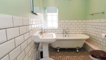 Un baño con azulejos blancos, una bañera, un inodoro y una ventana.