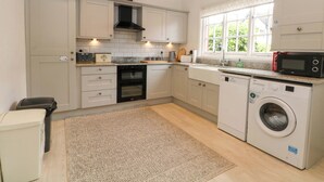 A modern kitchen with white cabinetry, a built-in oven, a microwave, and a washing machine. - Sunlight Soap Cottage (Wirral)