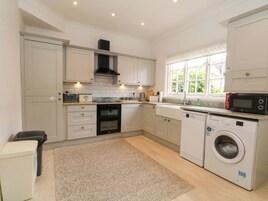A modern kitchen with white cabinetry, a built-in oven, a microwave, and a washing machine.