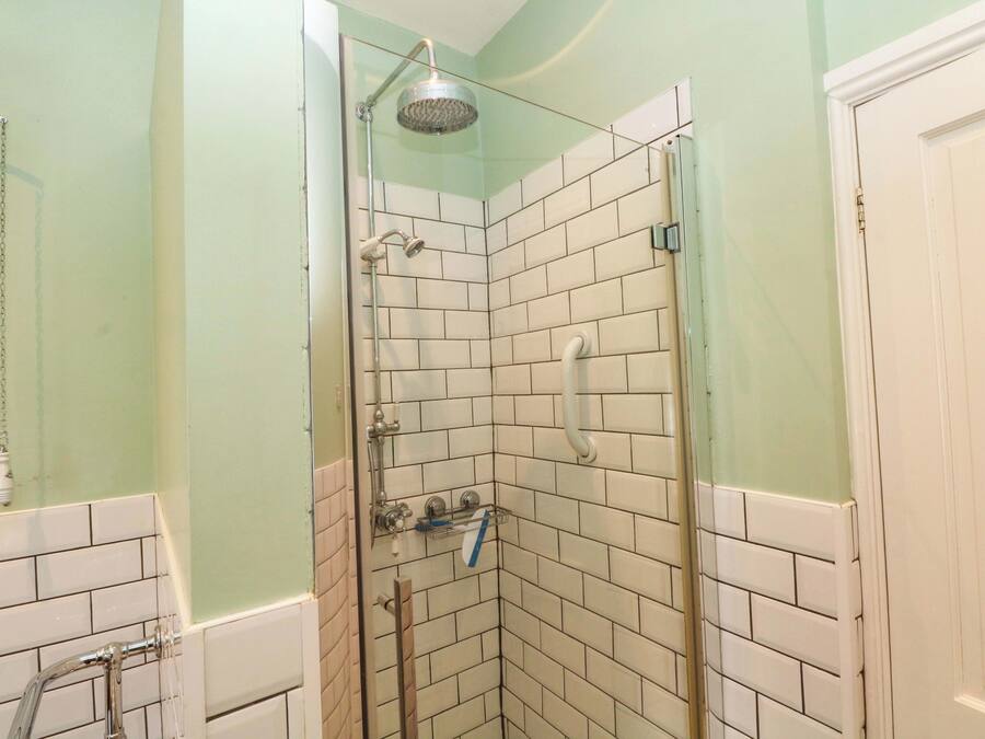 Ducha en esquina con azulejos blancos, puerta de vidrio y barra de apoyo.