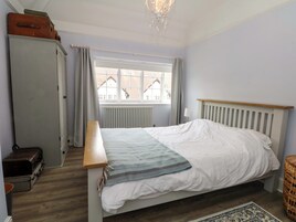 A bedroom with a bed, a dresser, a window with curtains, a radiator, and a chandelier.