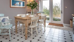 A dining area with a wooden table, white chairs, and a hexagonal tiled floor. - Maes y Cregyn (Marianglas)