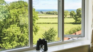 A window with binoculars on a windowsill, overlooking a green landscape with trees and fields. - Maes y Cregyn (Marianglas)