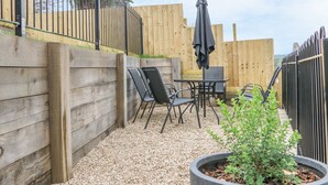 A patio area with a wooden fence, a table with chairs, and a potted plant. - Exmoor View (South Molton)