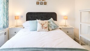 A neatly made bed with a dark headboard, two bedside lamps, and a wall-mounted picture frame with three heart-shaped decorations. - Exmoor View (South Molton)