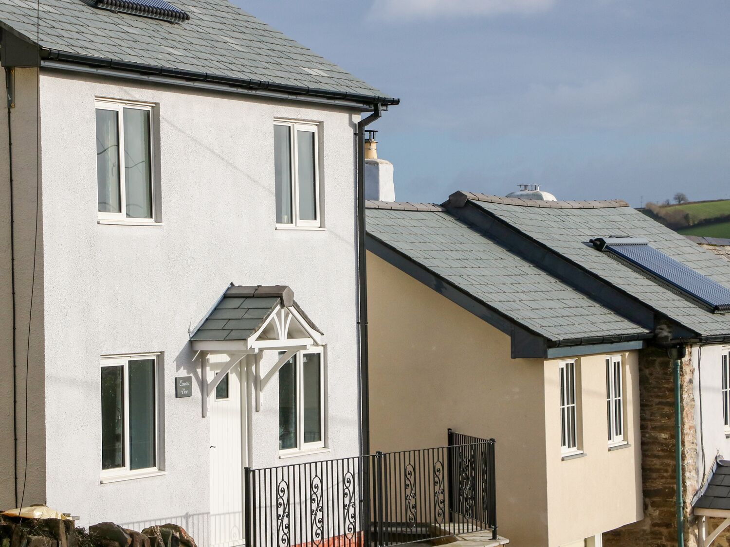 A row of white houses with grey roofs, featuring a small porch and a black metal fence.