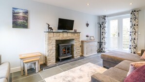 A living room with a stone fireplace, a television mounted above it, a bench, and a sofa. - Exmoor View (South Molton)