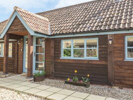 A wooden house with a tiled roof, a front door, and windows. There are flower beds with plants and flowers in front of the house.