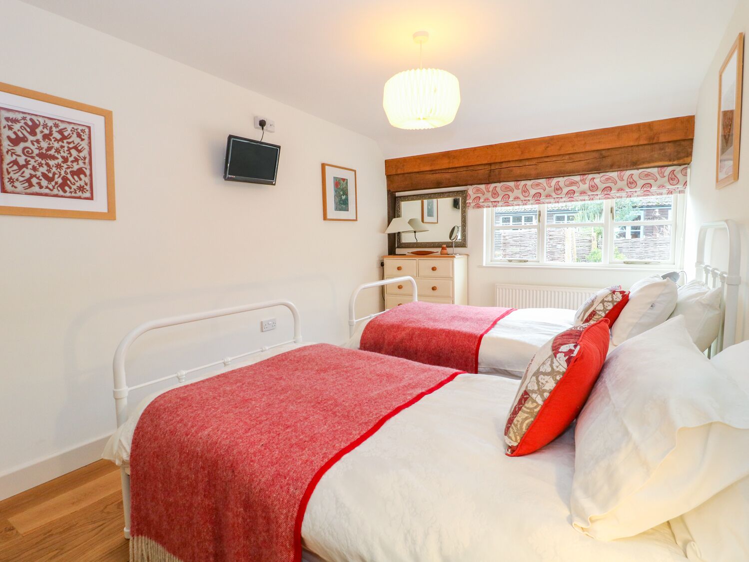 A bedroom with two beds, a television, a dresser, a window with a view, and a chandelier.