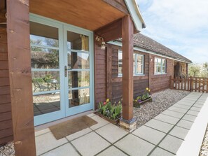 A wooden house with a covered porch, a sliding glass door, and a gravel pathway. - Shippon Barn (Yeovil)