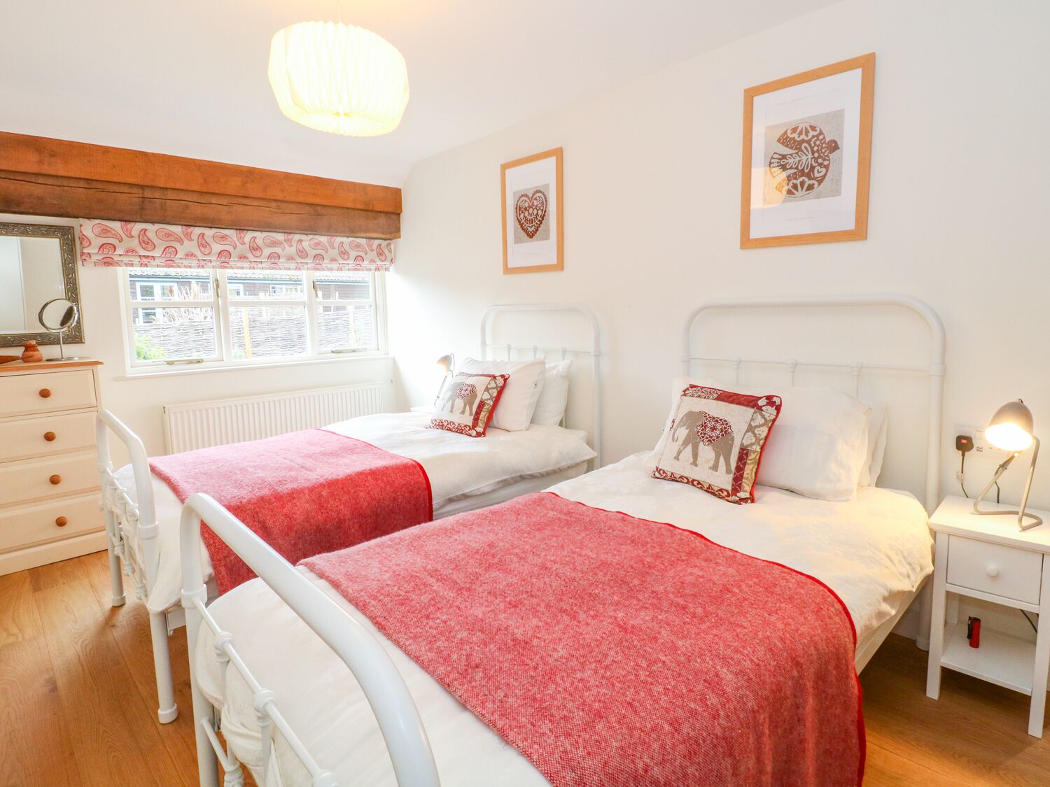 A bedroom with two beds, a dresser, a nightstand, and a window with a view.