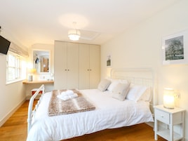 A bedroom with a bed, bedside table, nightstand, wardrobe, and a mirror.