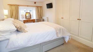 A bedroom with a bed, a dresser, a chair, a mirror, a wardrobe, and a television. - Greenham Cottage (Stoke-sub-Hamdon)