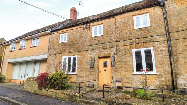 A two-story stone house with a garage, a wooden door, and a small garden area. - Greenham Cottage (Stoke-sub-Hamdon)